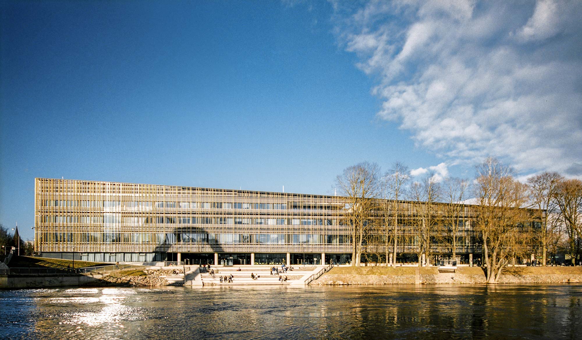 Large building in Tartu Estonia with golden front facing the river and a sitting area below