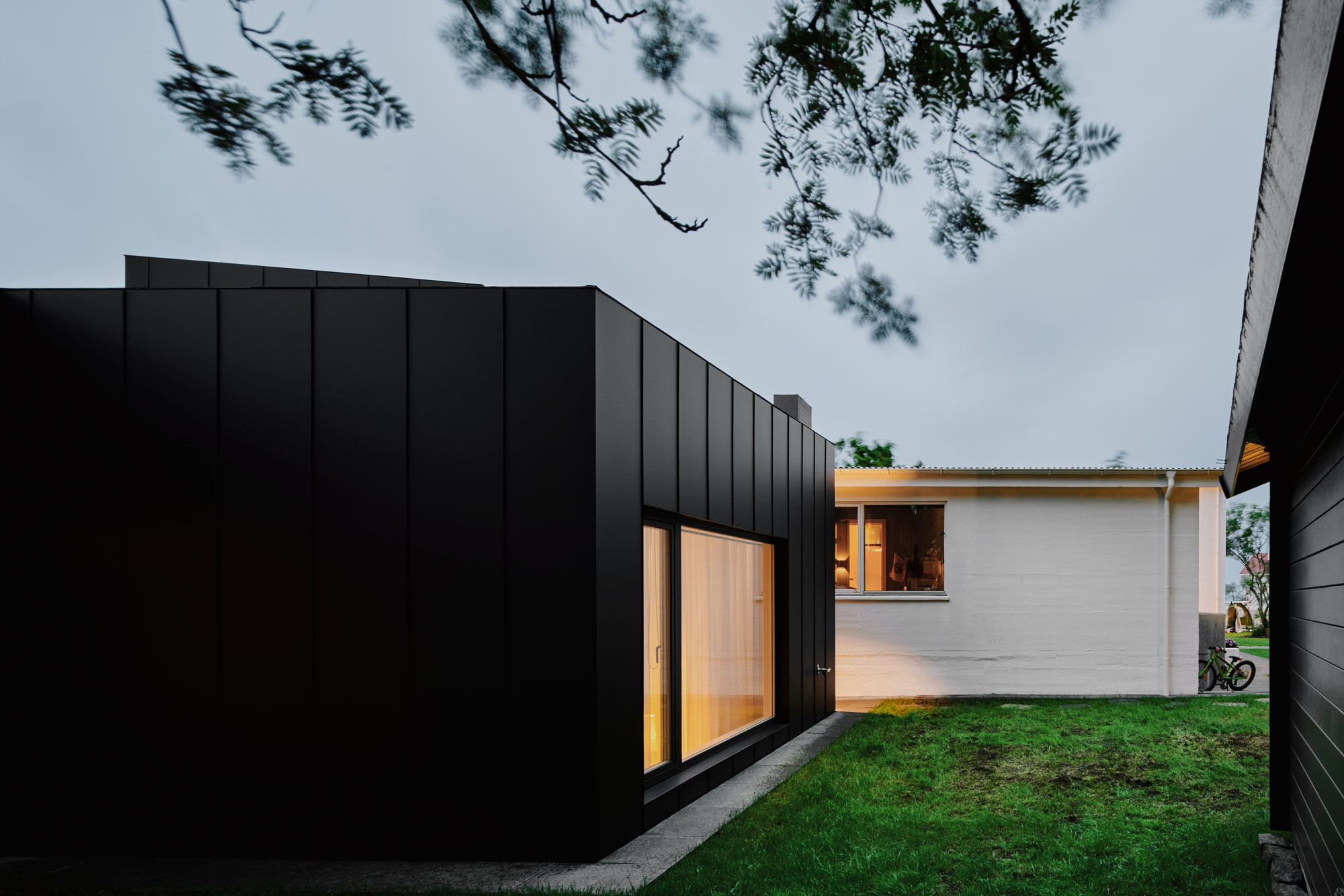 Black metal cladding home with large windows and green grass garden