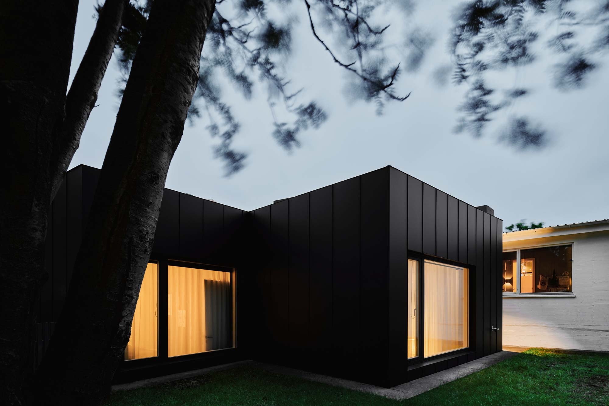 Black house metal cladding large windows twilight moody interior